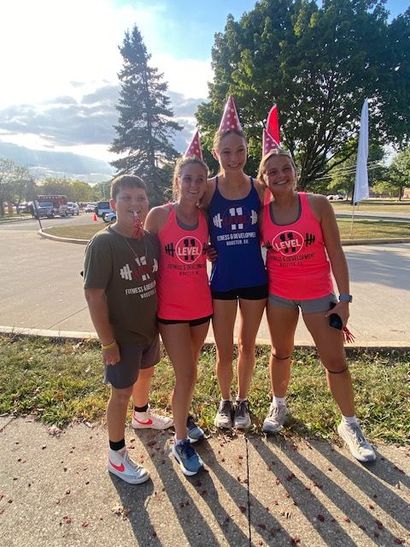 Four people wearing athletic gear and party hats pose outdoors.
