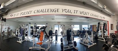 Gym interior with exercise machines and motivational quote on the wall.