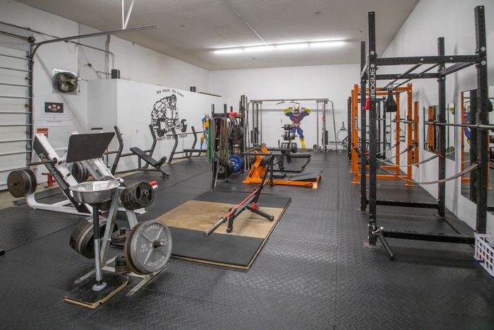 Home gym with various weightlifting equipment on a black rubber floor.