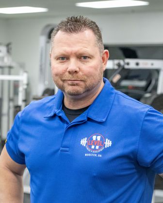 Man in blue polo shirt at a gym, arms crossed, looking at the camera.