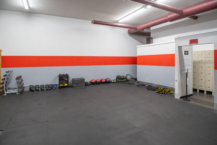 Gym interior with weights, kettlebells, and lockers against red, gray, and white walls.