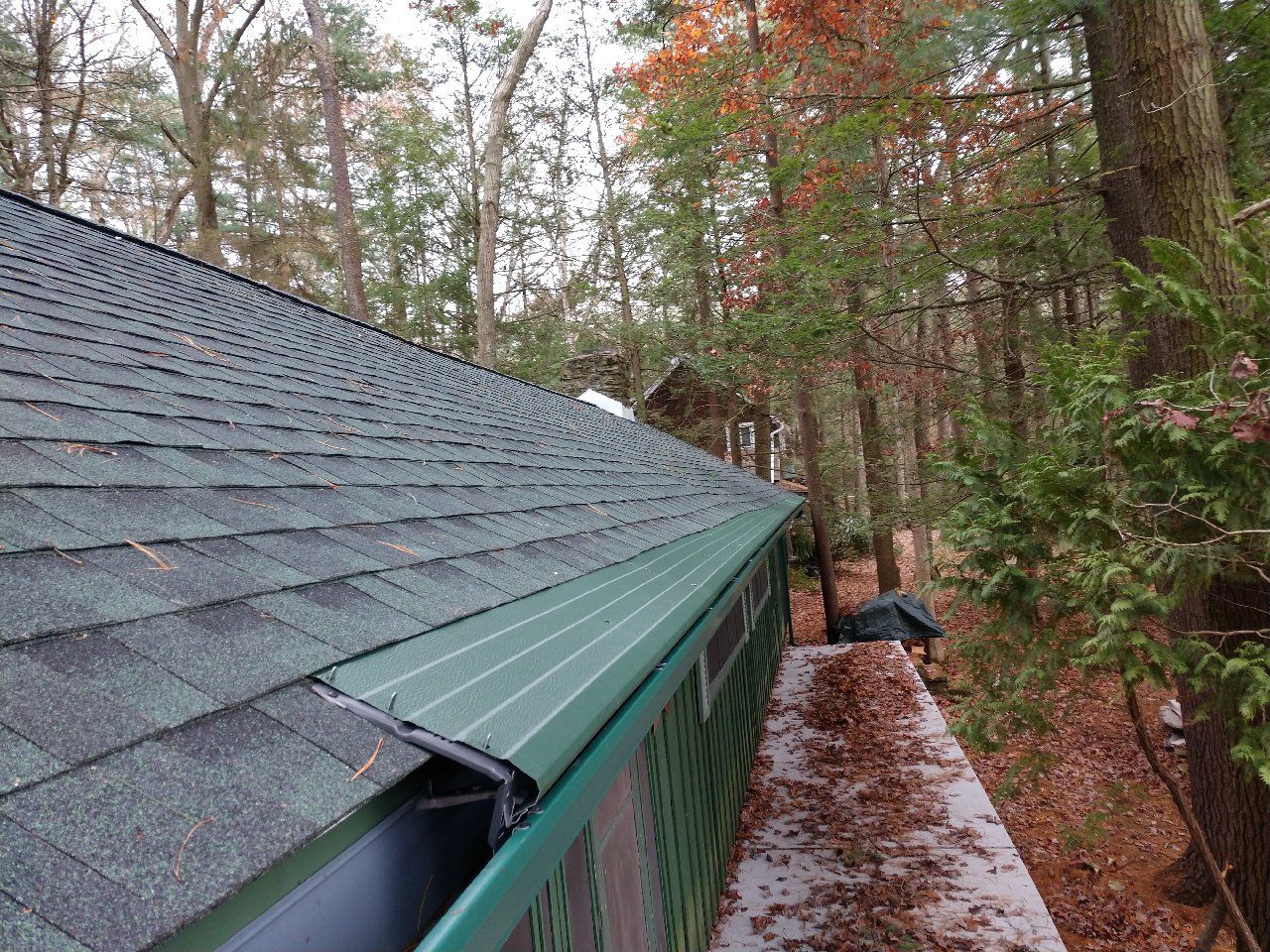 A roof with a green gutter and trees in the background