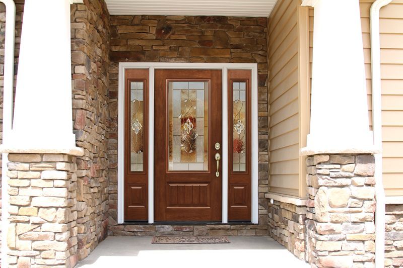 Brown front door with decorative glass panels, flanked by stone columns on a porch.
