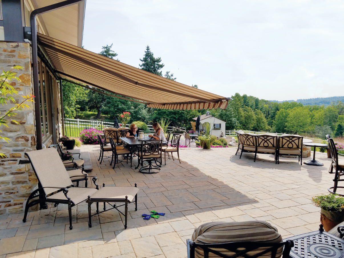 Patio with awning, furniture, and a view of trees and sky.