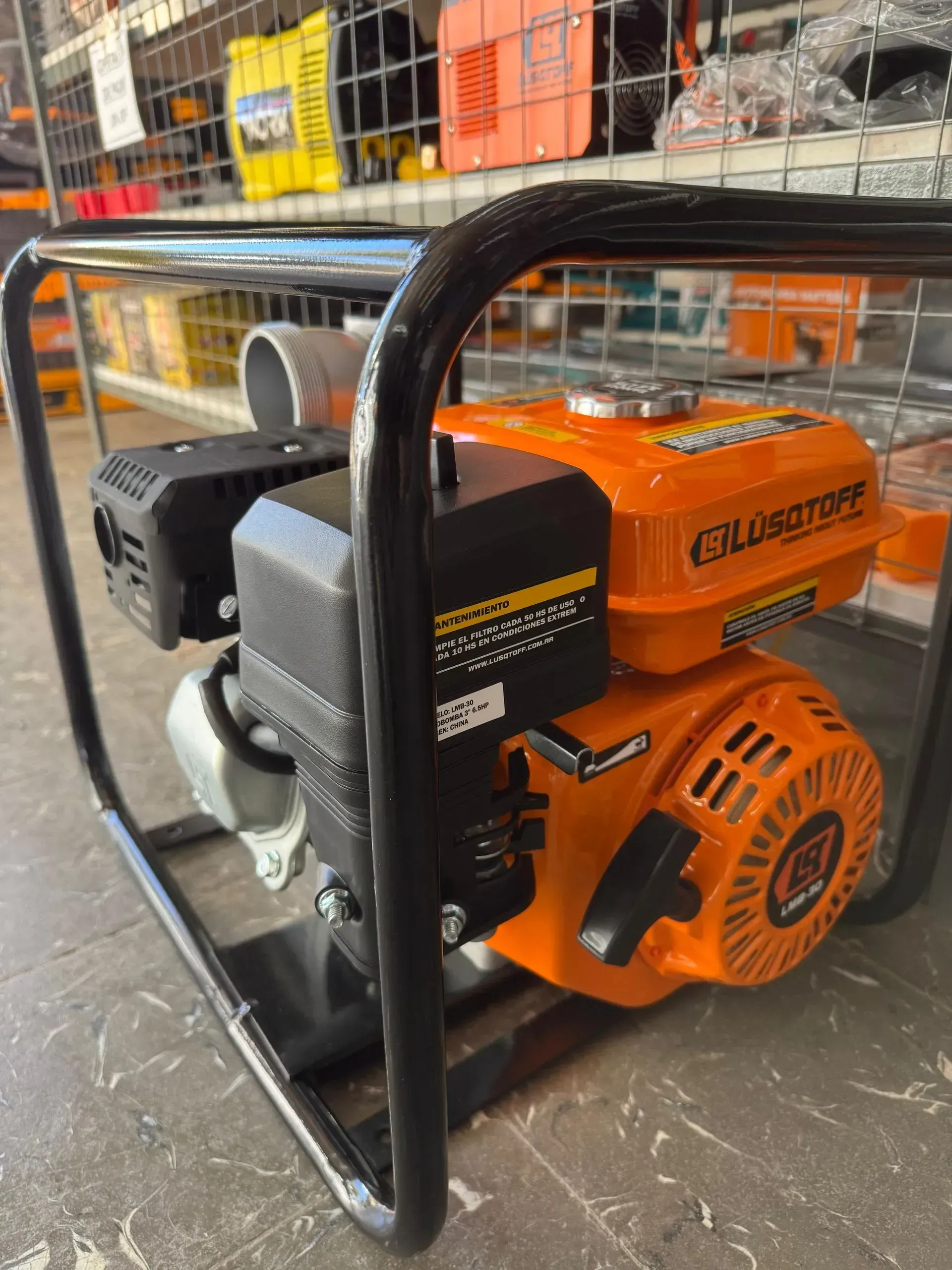 Generador portátil naranja en una estructura de metal negro en el suelo de una tienda, con estanterías al fondo.