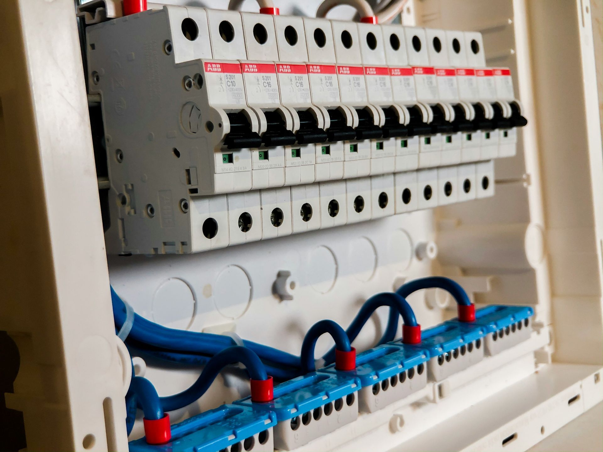 Panel de disyuntores eléctricos con filas de interruptores y cableado azul dentro de una caja.