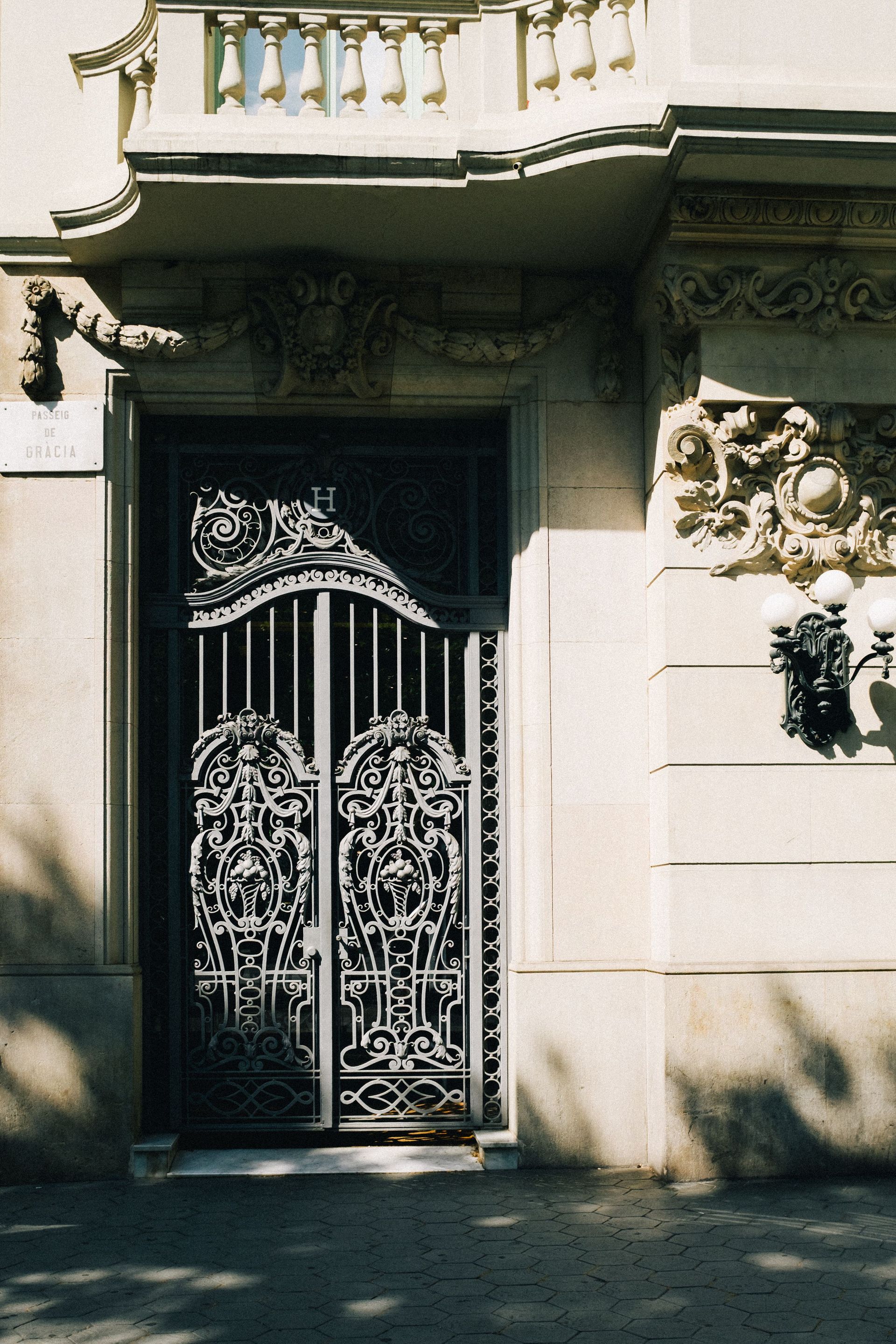 Elegante verja de hierro forjado negro en la entrada de un edificio soleado con fachada de piedra y balcón