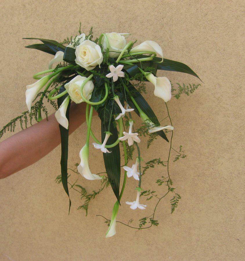 Mano che regge un bouquet di fiori bianchi a cascata: rose, calle e gelsomino su uno sfondo beige.