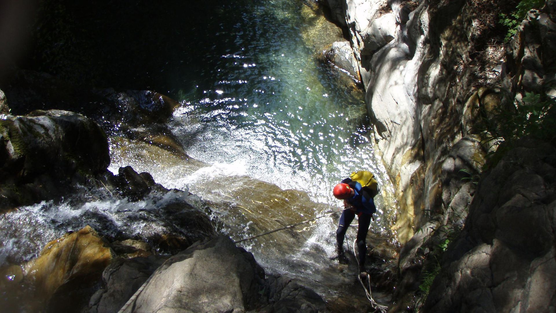 Persona haciendo rápel por una cascada rocosa hasta una piscina de agua clara.