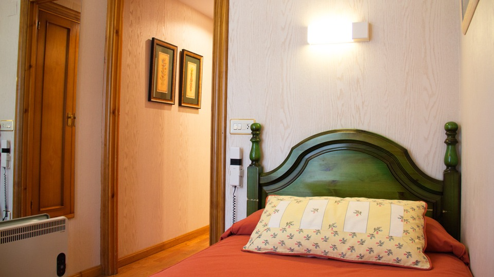 Marco de cama verde, colcha naranja, almohada amarilla en un dormitorio pequeño con puerta.