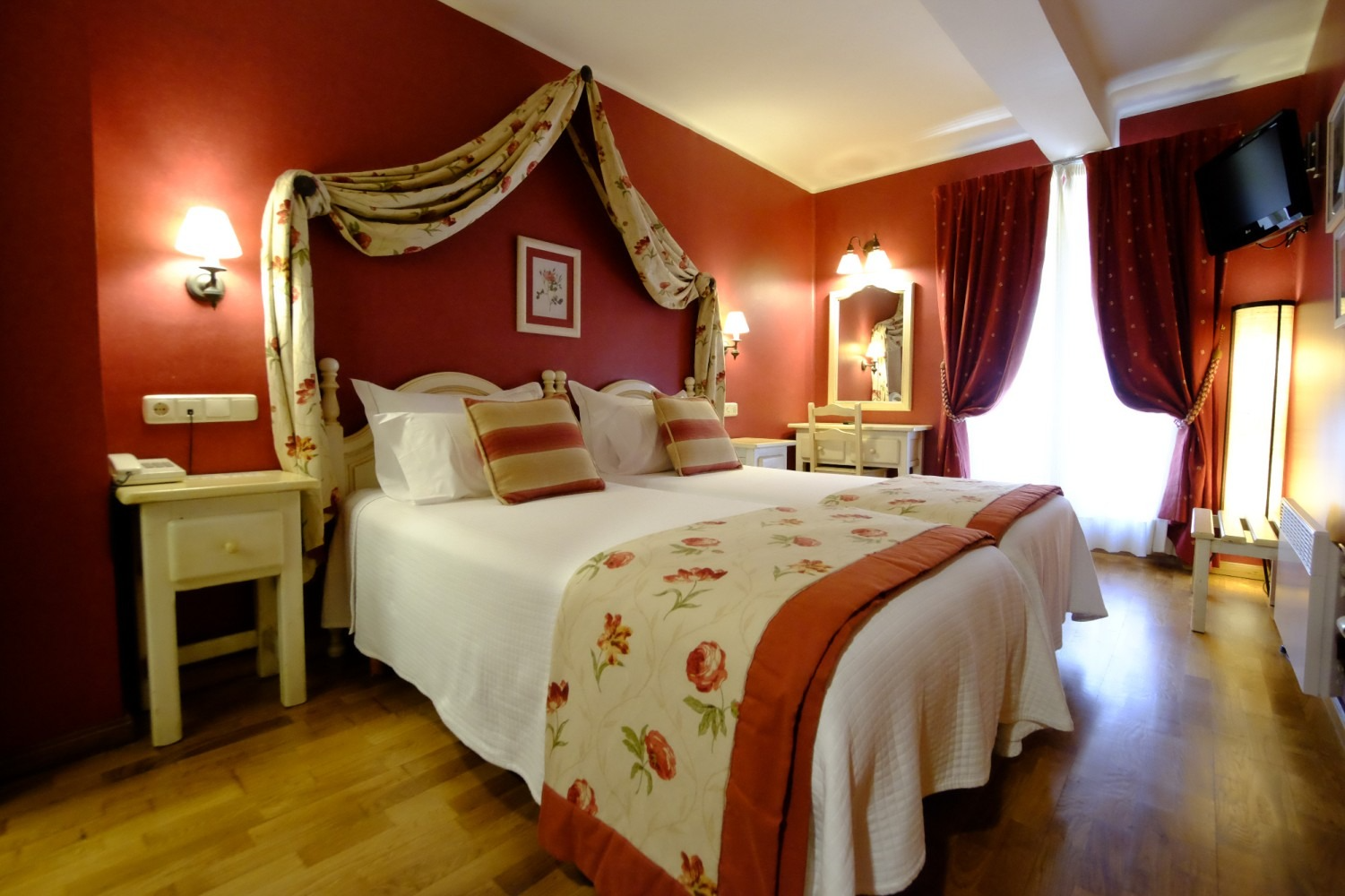 Dormitorio con pared roja, cama con dosel, ropa de cama blanca y mesita de noche de madera.