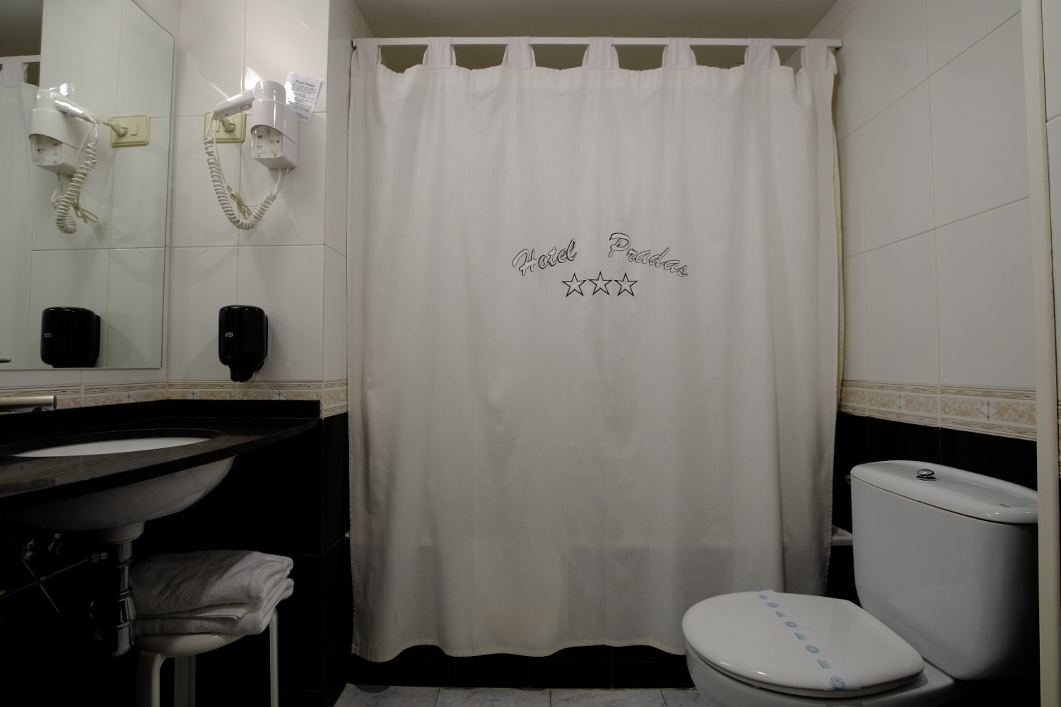 Baño con cortina de ducha, inodoro, lavabo, espejo y secador de pelo.