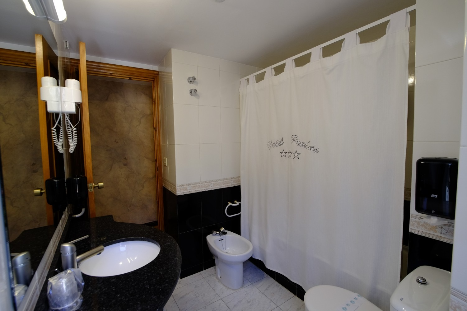 Baño con azulejos en blanco y negro, cortina de ducha, inodoro y lavabo.