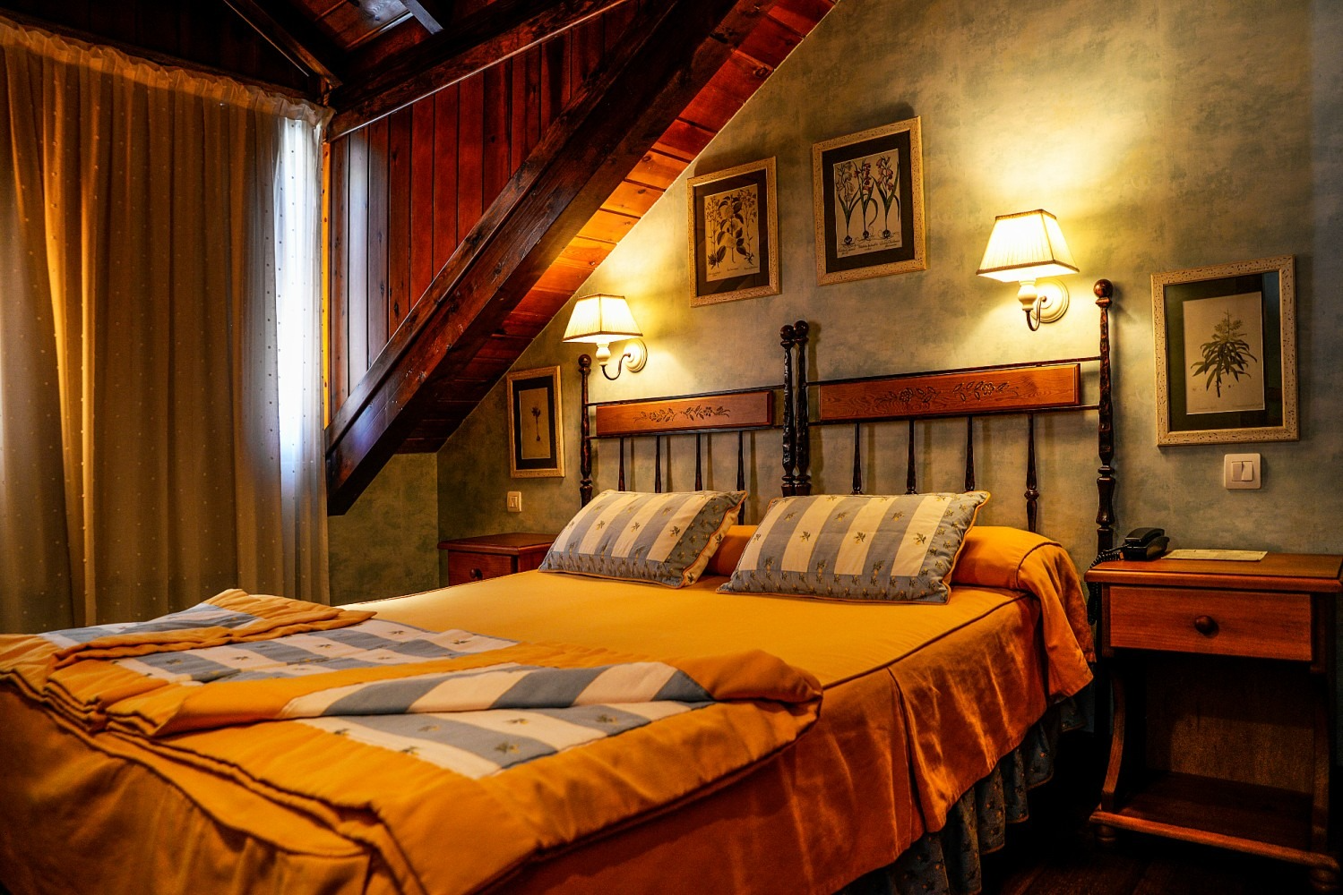 Dormitorio con techo y cabecero revestidos de madera. Ropa de cama amarilla, dos almohadas, dos apliques de pared.