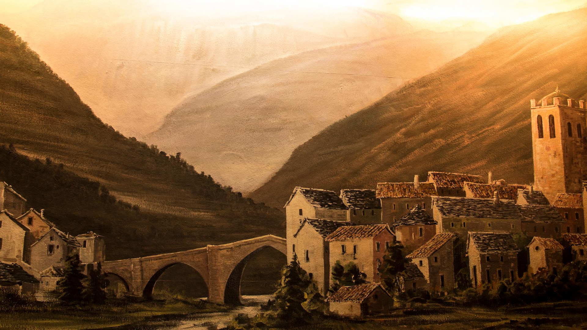 Un pueblo con edificios de piedra y un puente arqueado enclavado en un valle entre montañas marrones bajo un cielo dorado.