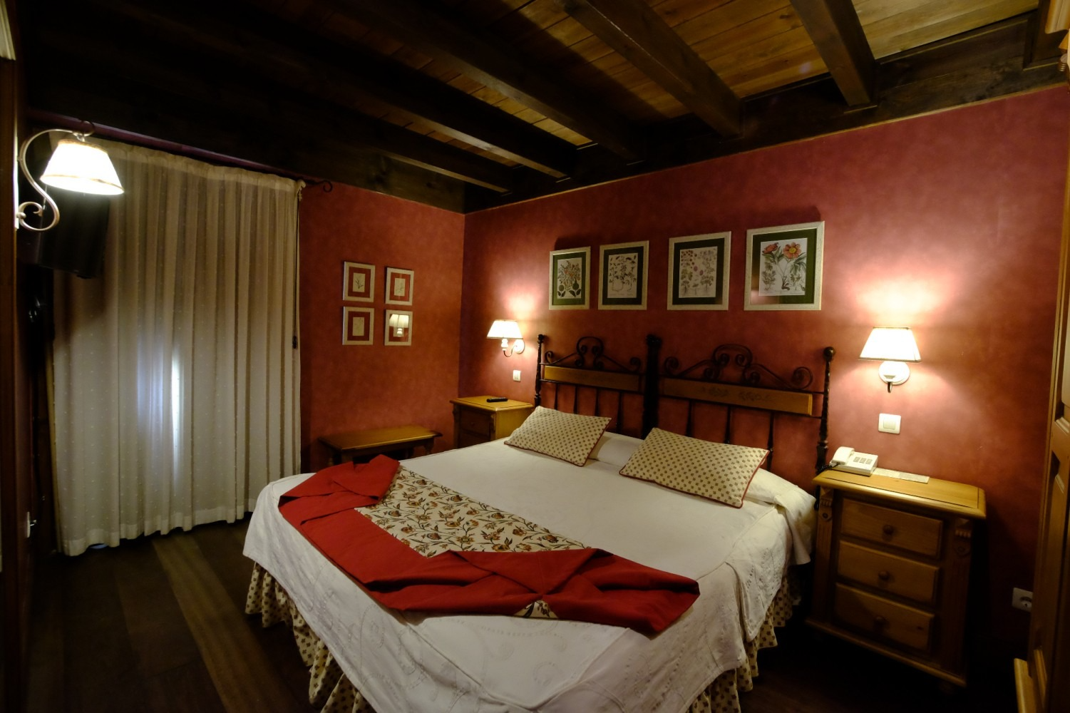 Dormitorio con paredes rojas, marco de cama de madera, ropa de cama blanca y dos mesitas de noche.
