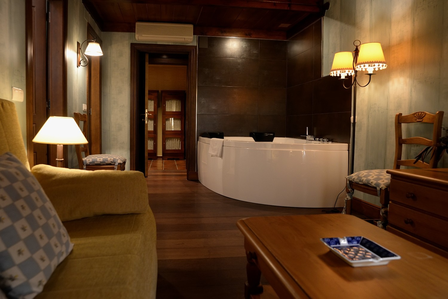 Acogedora habitación de hotel con jacuzzi, sofá, mesa y suelo de madera oscura.