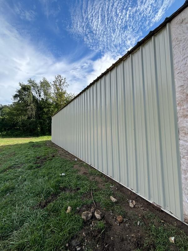 Long beige metal building wall beside grass under a blue sky with clouds
