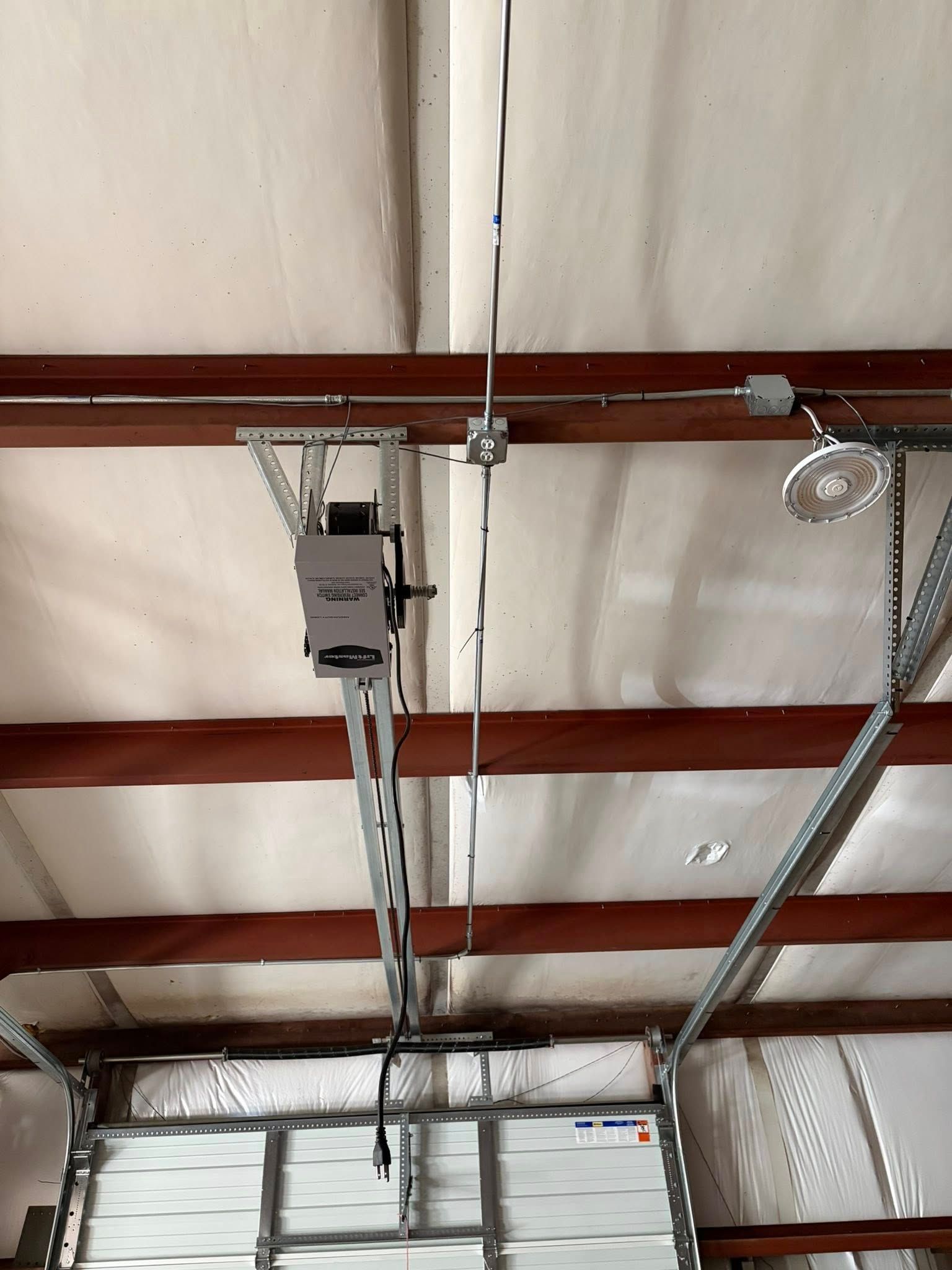 Garage ceiling with exposed beams, garage door opener, and metal tracks hanging overhead