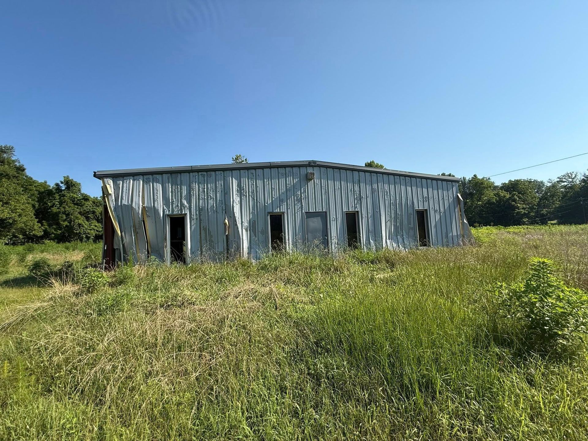 Weathered metal shed in a grassy field under a clear blue sky.