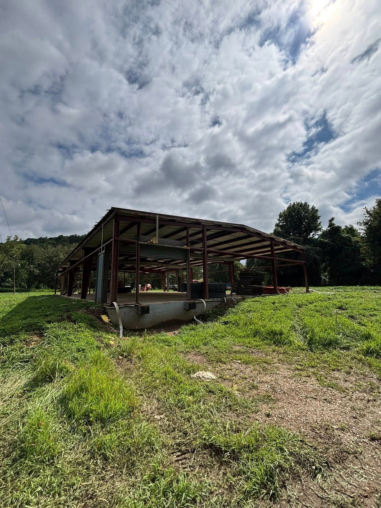 Open-sided barn in a green field under a cloudy sky