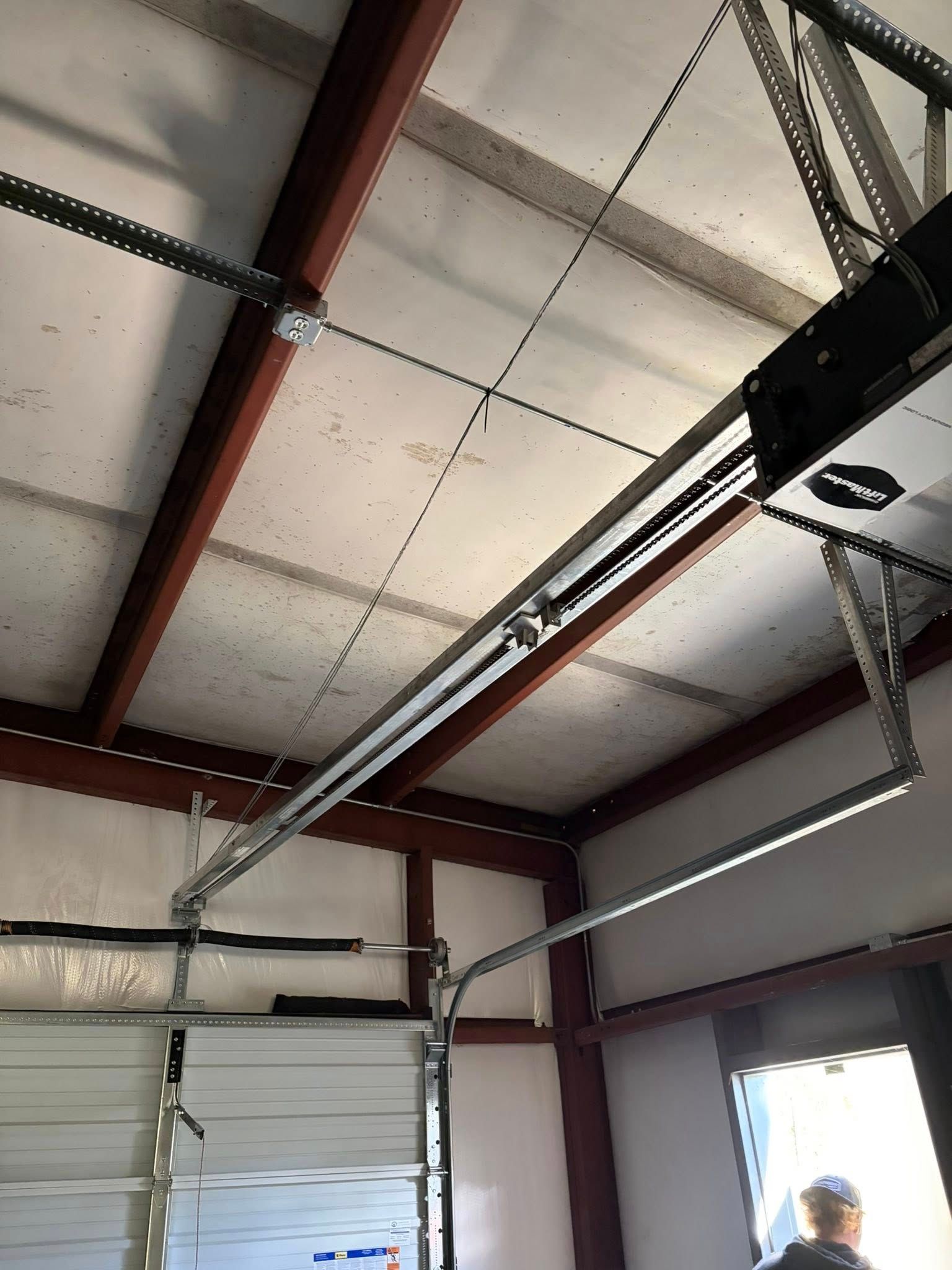 Interior of a warehouse ceiling with steel beams, overhead garage door tracks, and a person near the bottom right