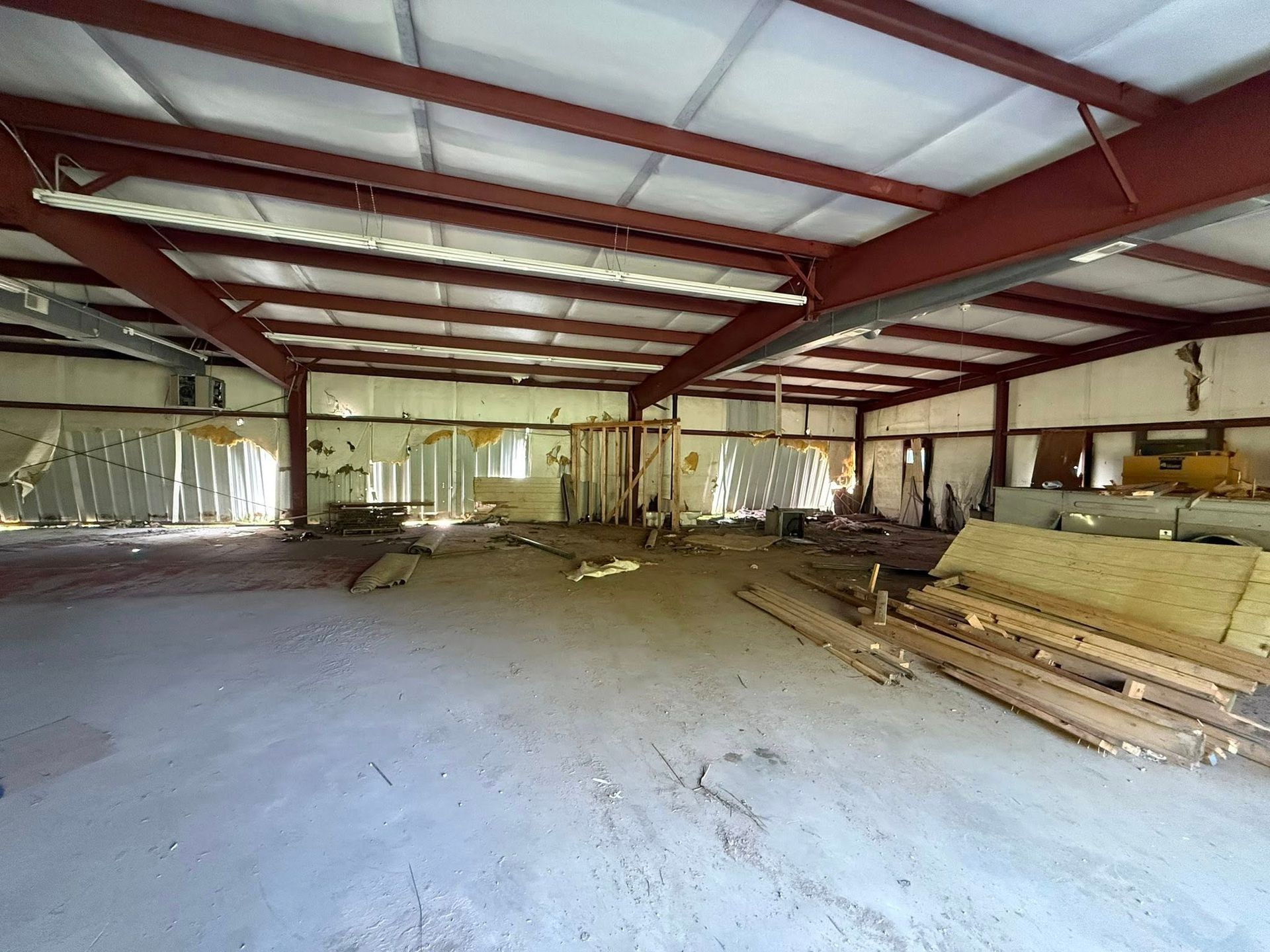 Empty industrial warehouse with steel beams, unfinished walls, and stacked lumber on the right