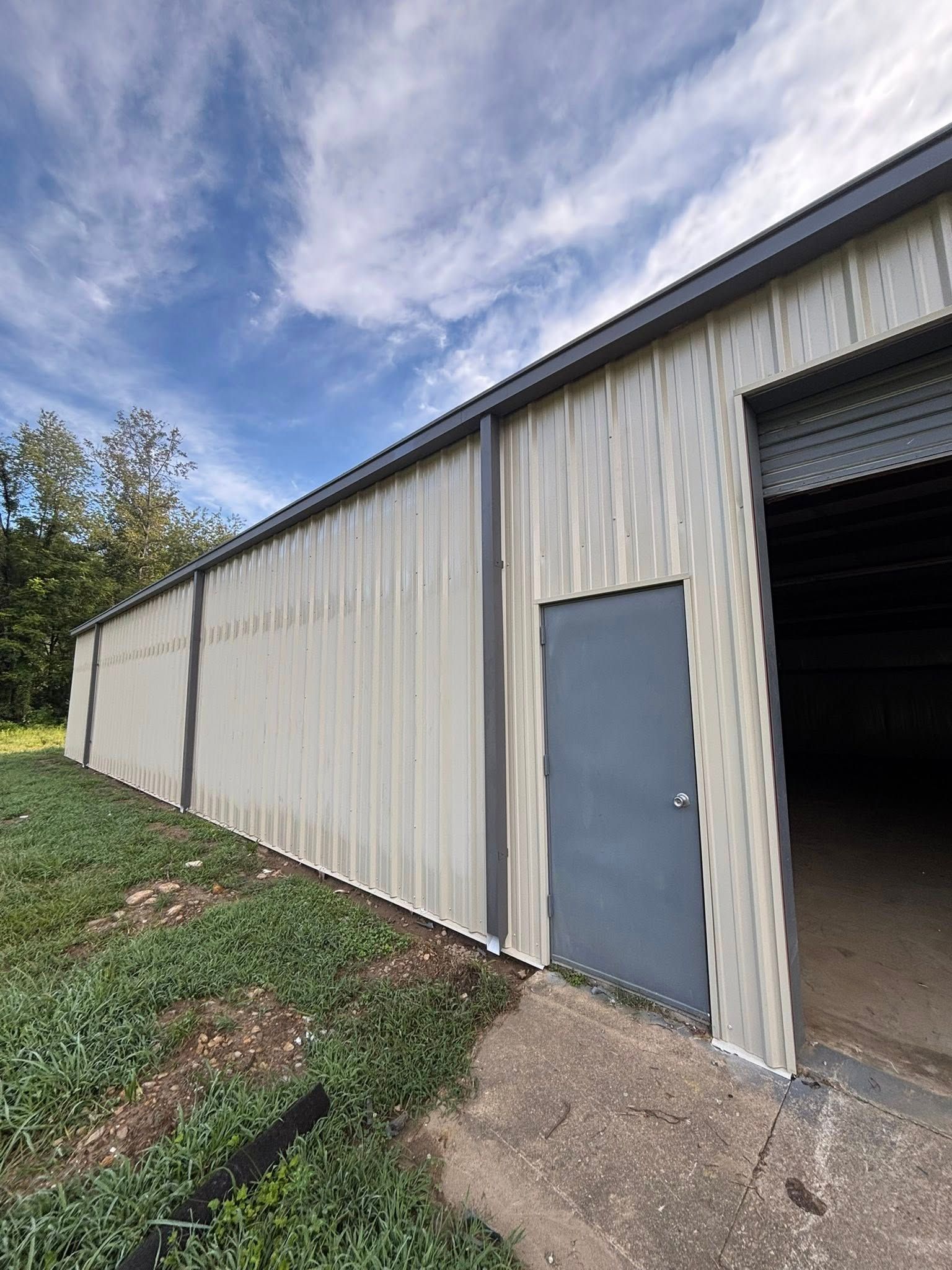 Long white metal building with gray door and open garage bay under a cloudy sky.