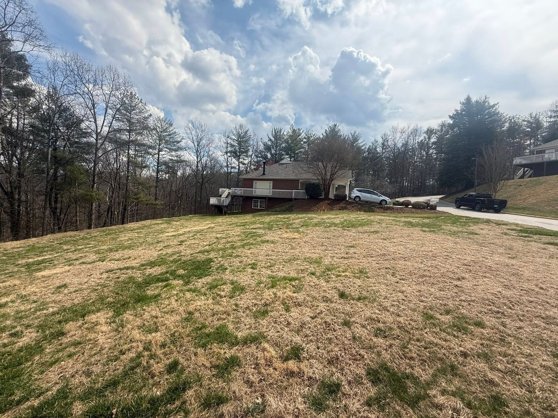 Grassy hillside leading to a house under a cloudy sky, with trees lining the background.