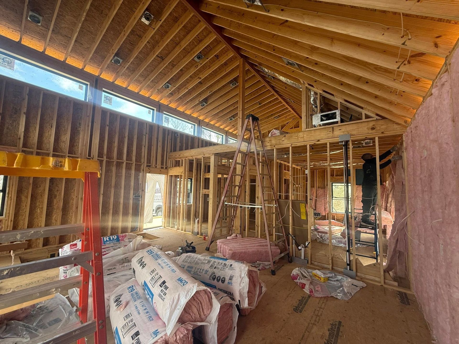 Unfinished room interior with exposed wood framing, vaulted ceiling, insulation rolls, and construction materials on the floor