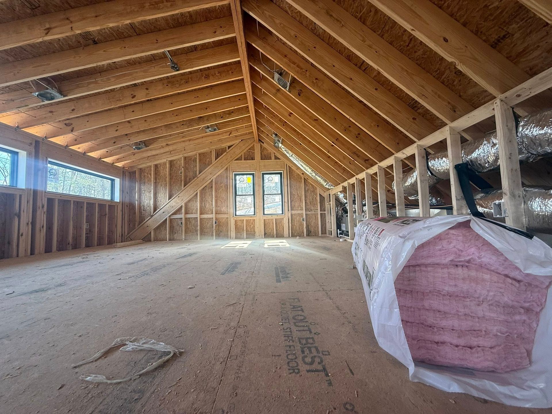 Unfinished attic interior with exposed wooden rafters and insulation materials on the floor and right side.