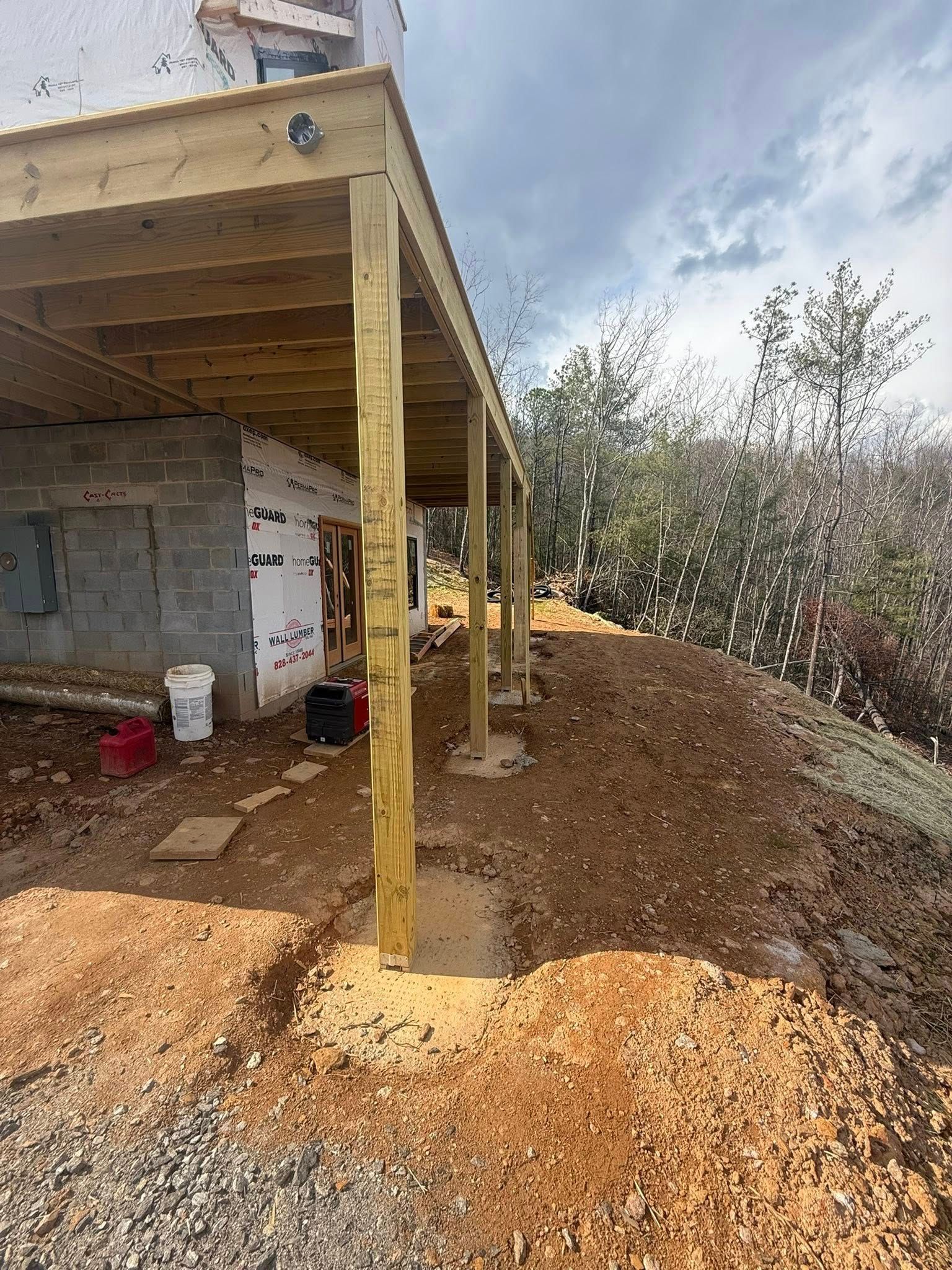 Partially built wooden porch beside a white house, with dirt and gravel piled around it.