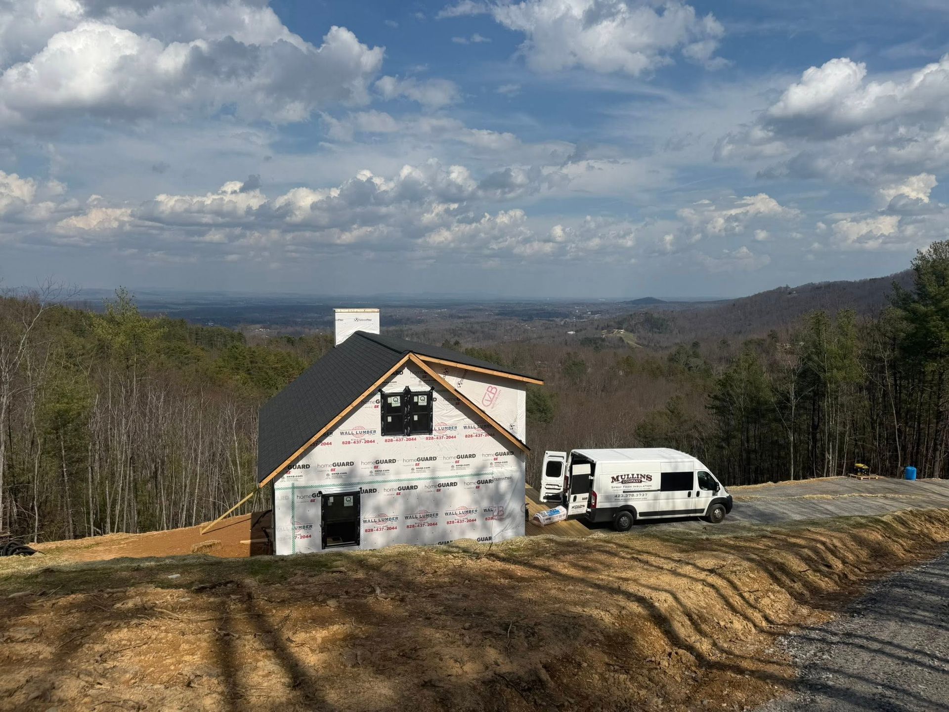 Small white house under construction on a hillside with a white van and cloudy sky.
