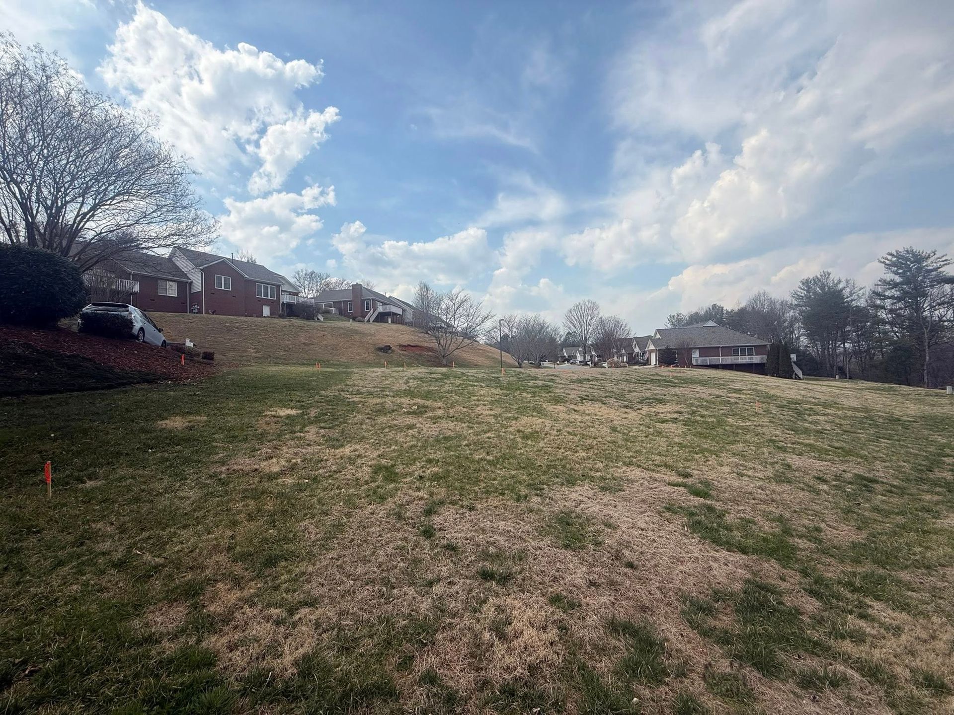 Grassy hill under a partly cloudy sky, with houses and trees along the horizon.