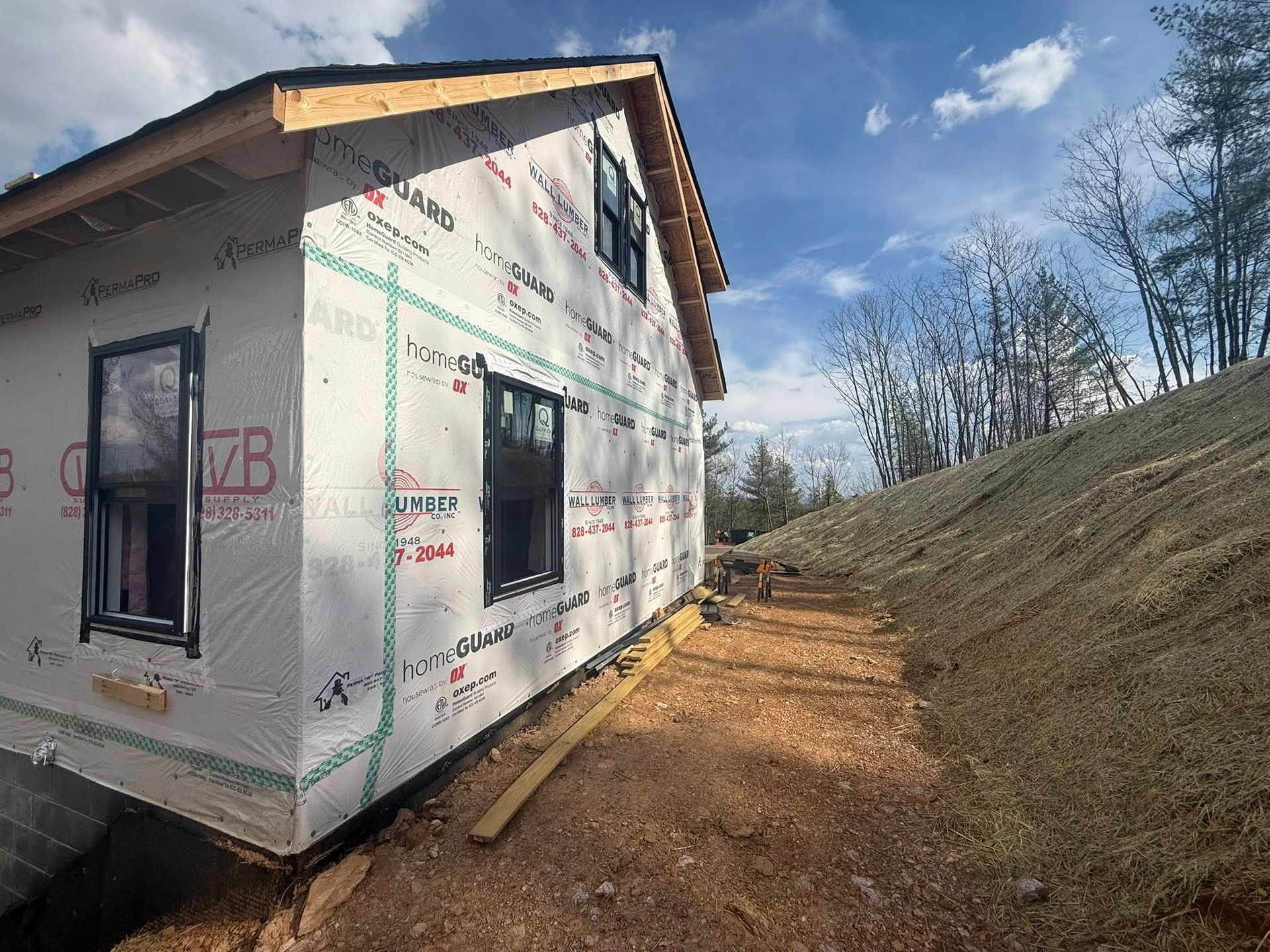 Partially built house wrapped in white house wrap beside a dirt path on a sunny hillside