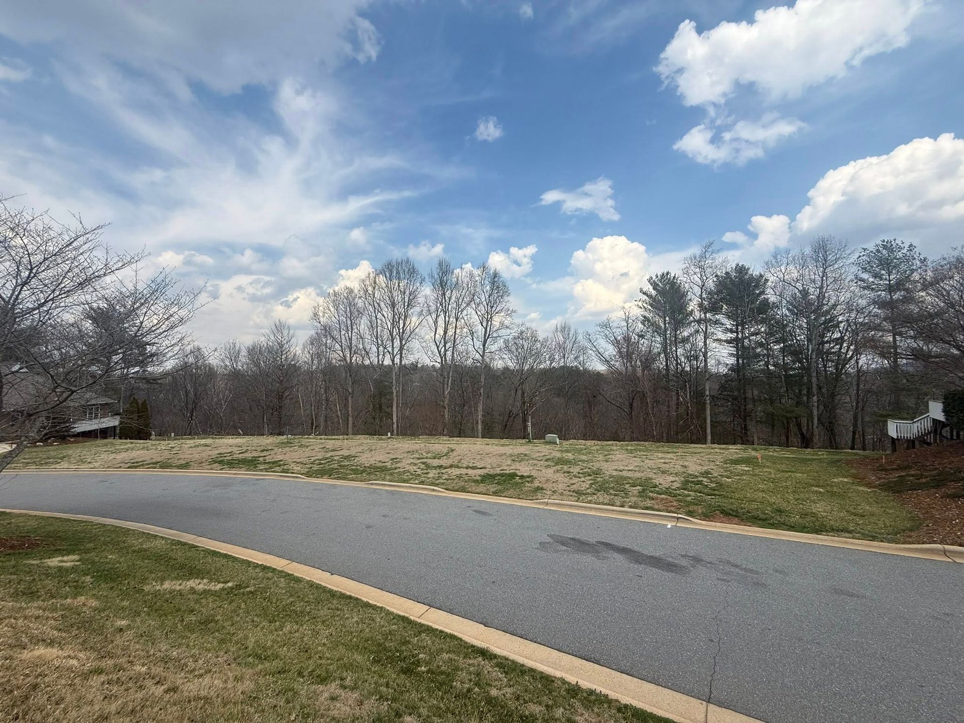 Curved paved path beside grass and bare trees under a partly cloudy blue sky