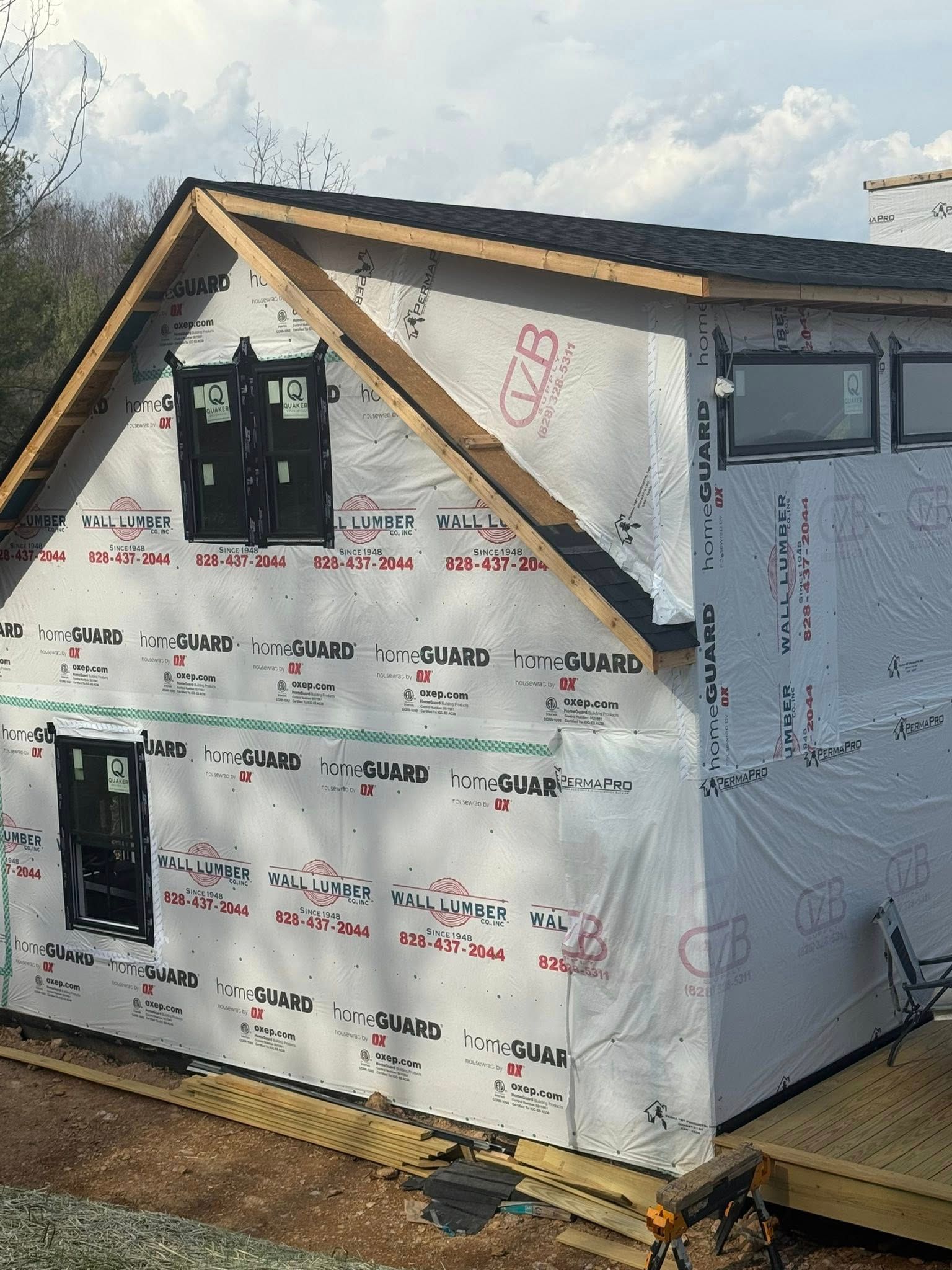 Small house under construction, wrapped in white house wrap with black-framed windows and dark roof shingles.