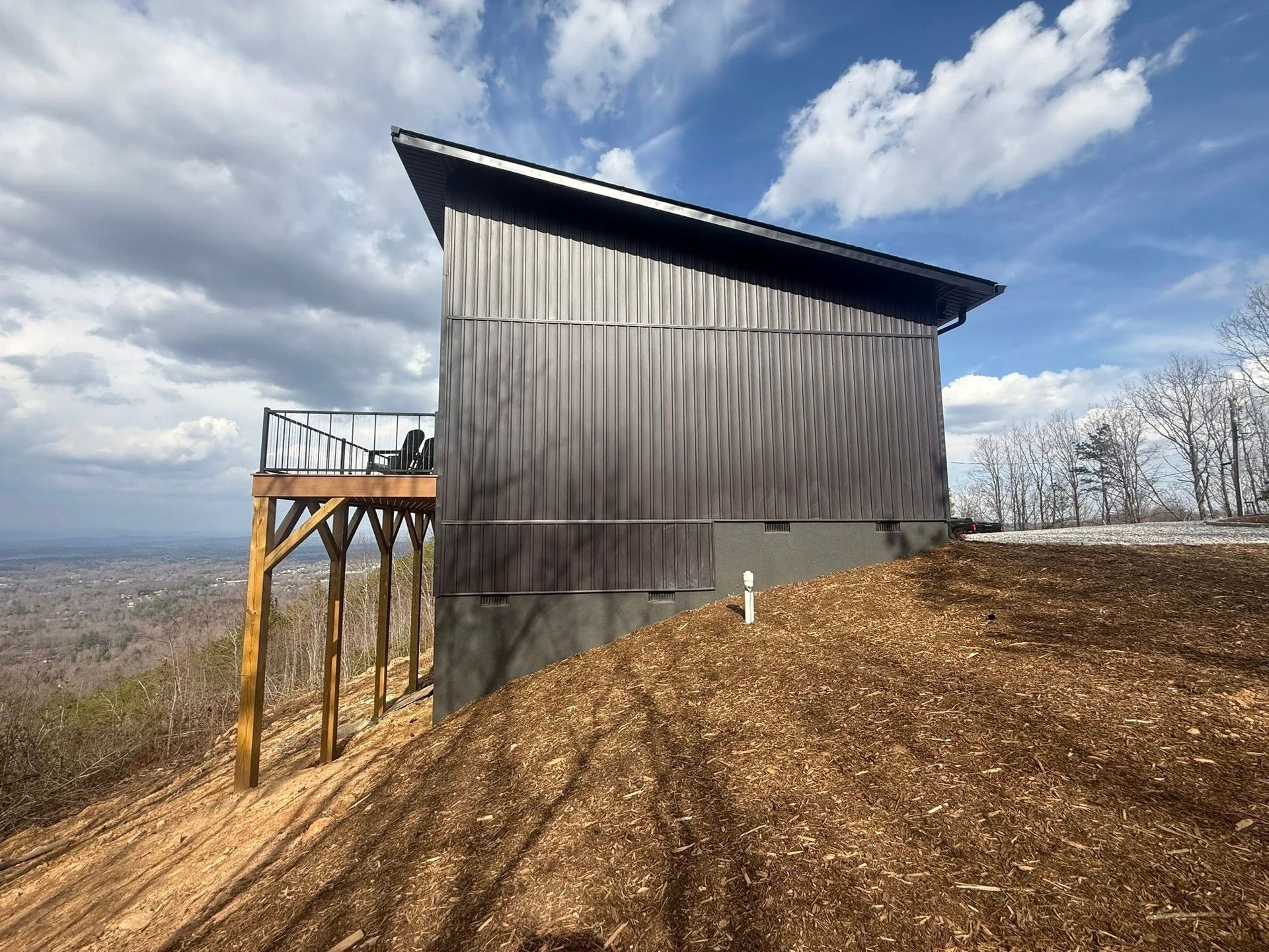 Wood-sided lookout tower on a hill under a partly cloudy sky, with bare trees and a wooden platform walkway