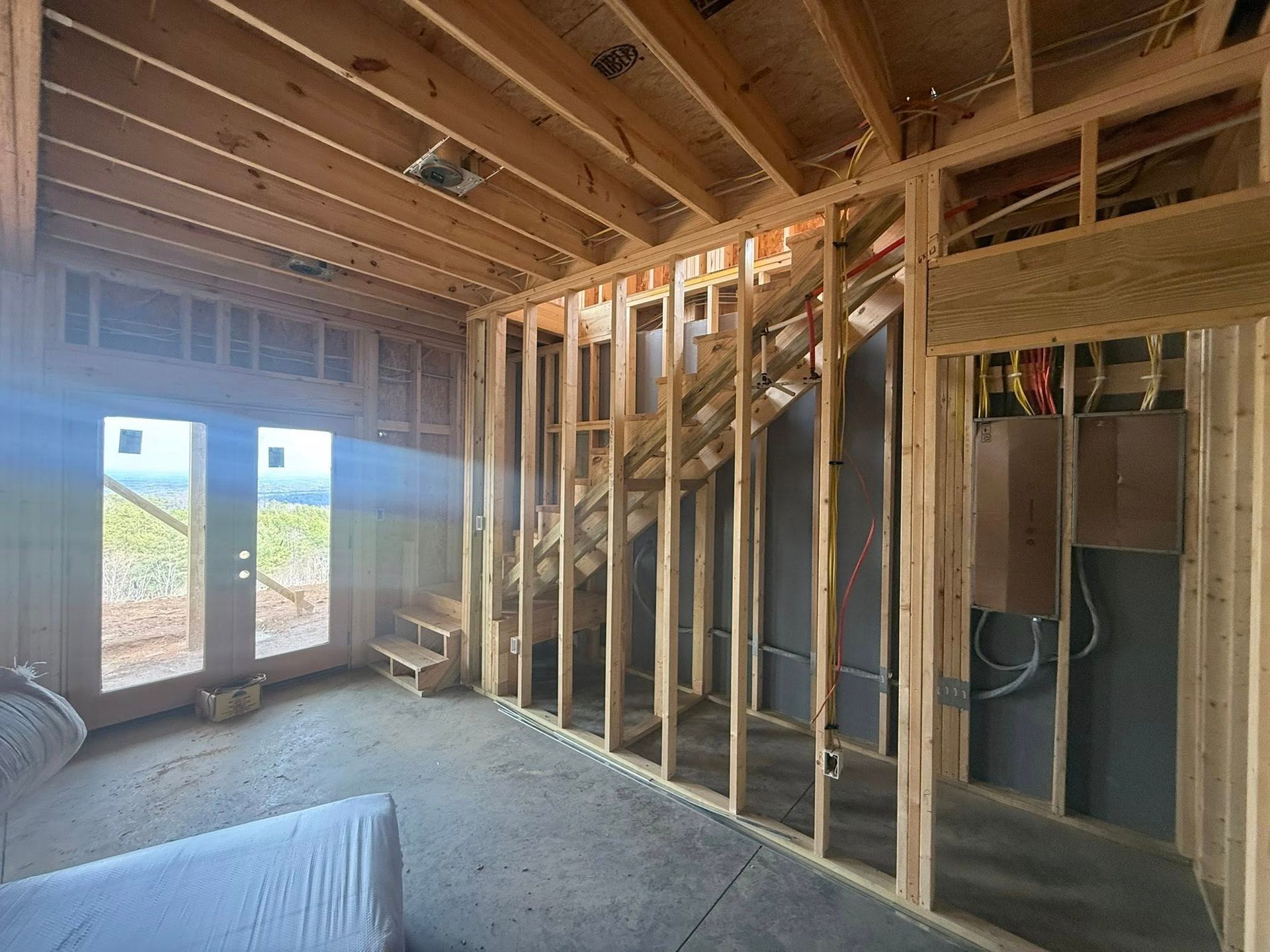 Partially framed room with exposed studs, wooden ceiling joists, and windows under construction