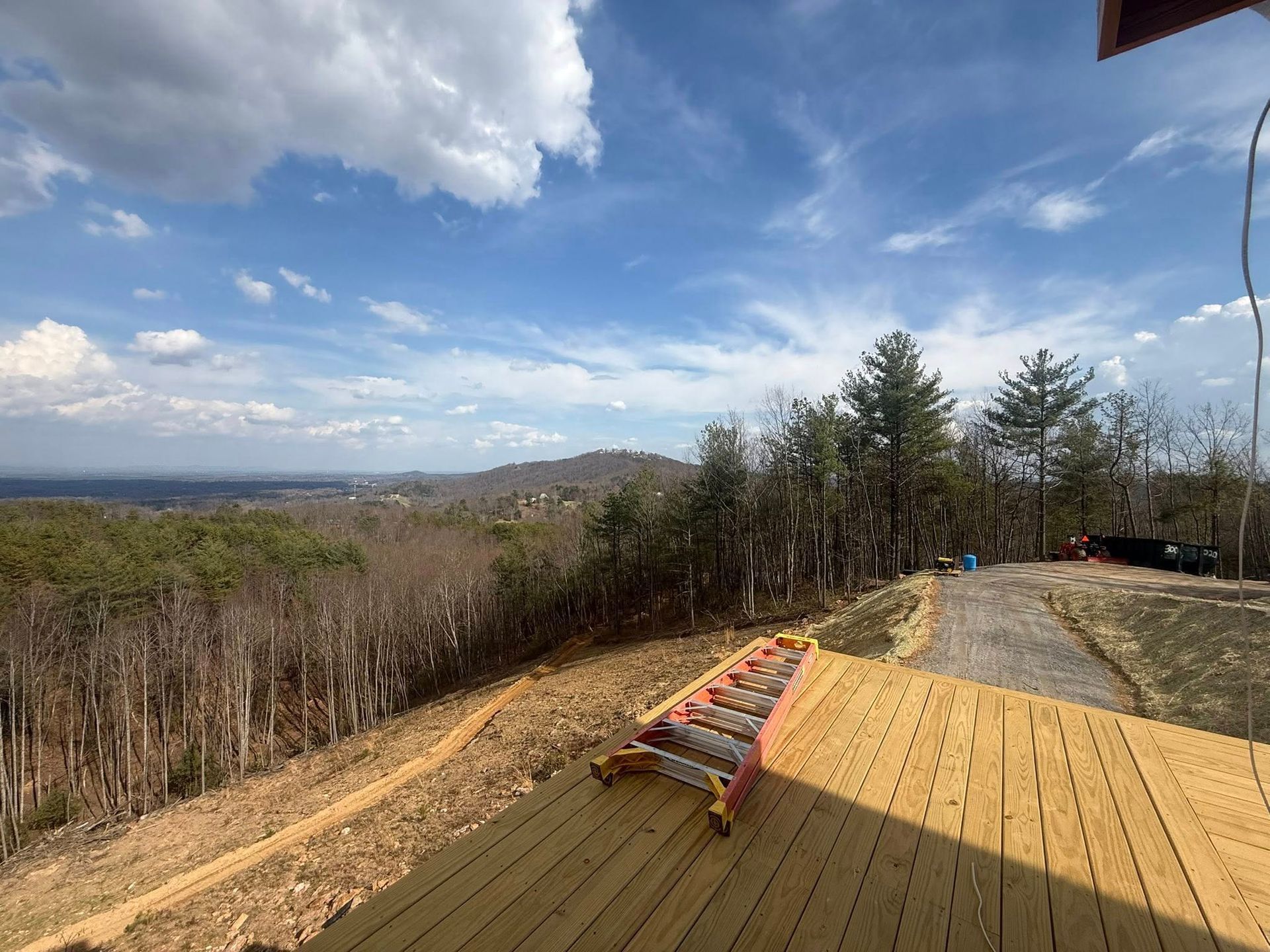 Wooden deck with a bench overlooking a wooded valley under a blue sky with clouds