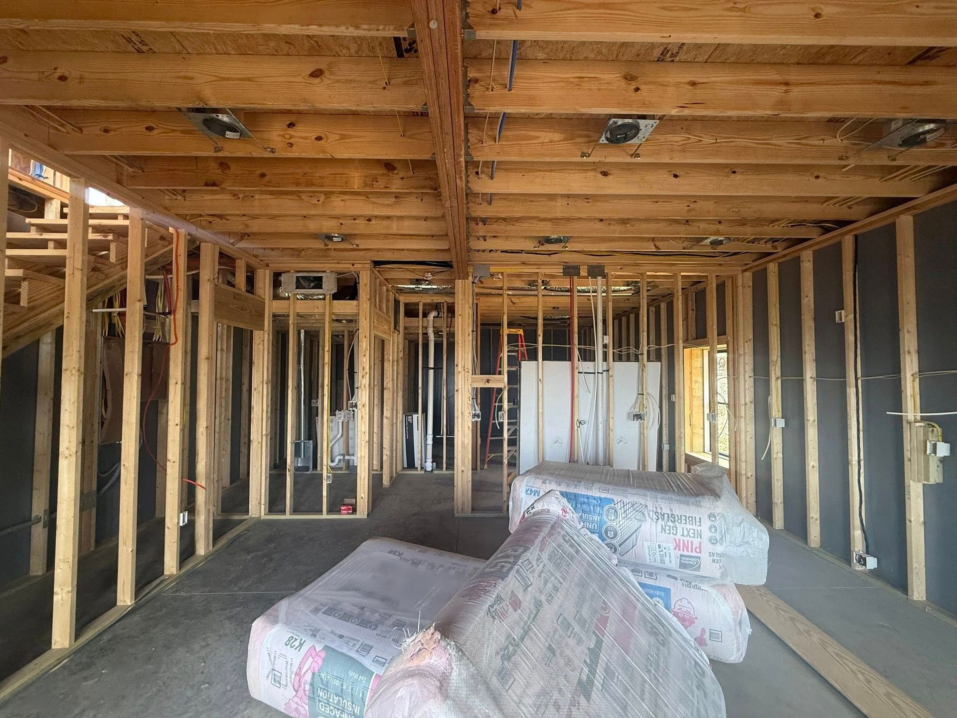 Interior of a house under construction with exposed wood framing and insulation bundles on the floor