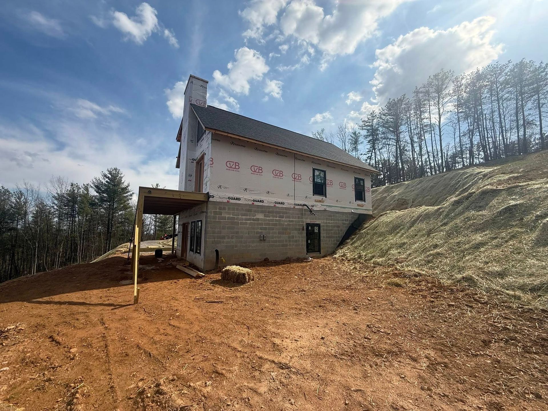 Damaged two-story house on a dirt slope under a cloudy sky, with a small porch and bare trees nearby