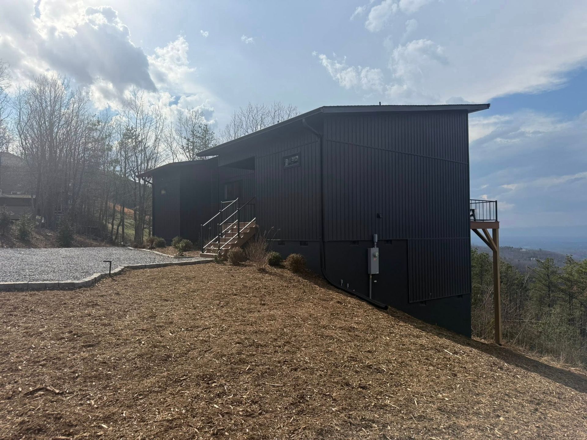 Dark wooden cabin on a rocky hillside with bright sky and leafless trees in the background