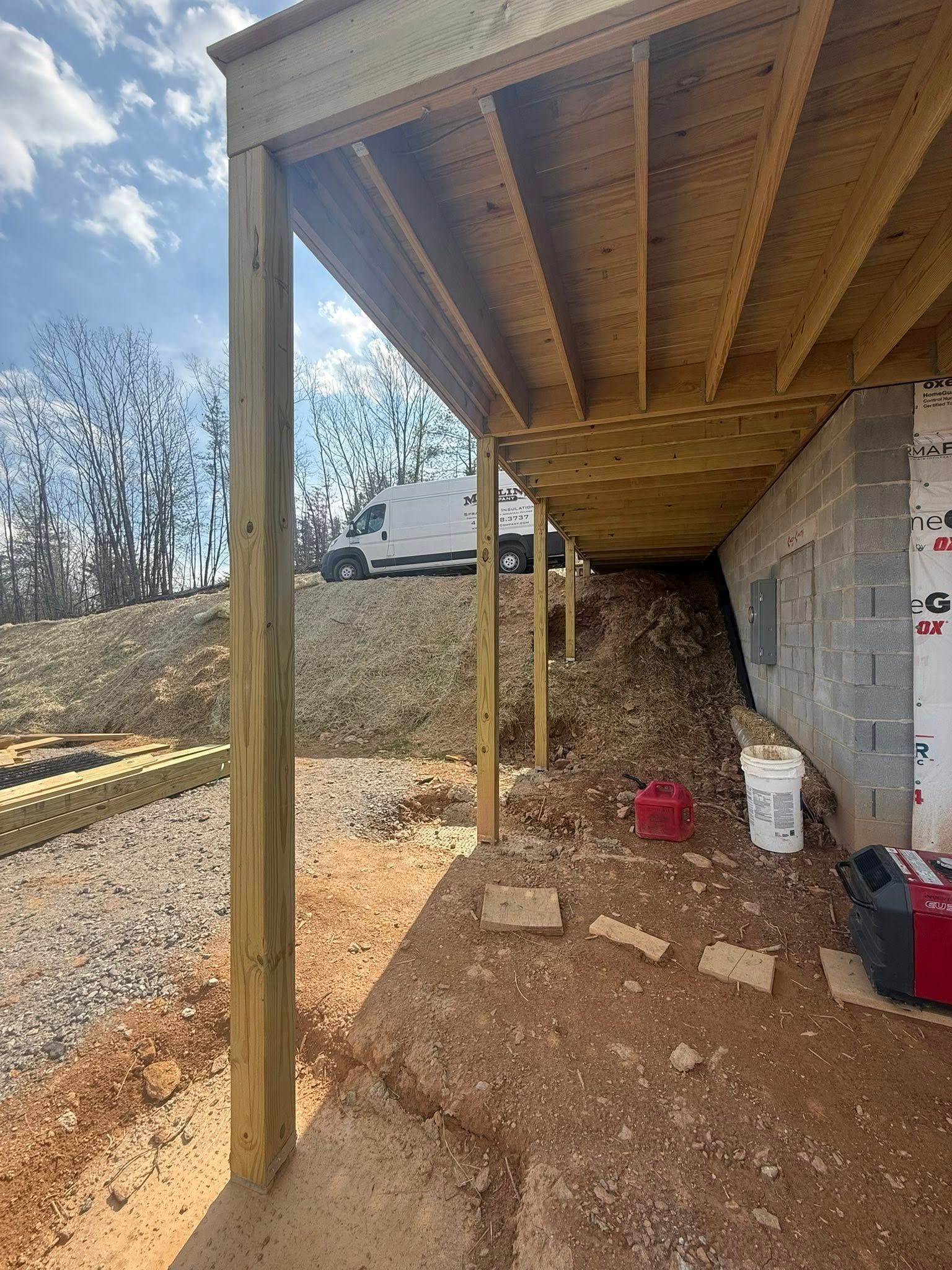 Under-deck storage area with dirt floor, wooden posts, and buckets beside a house wall.