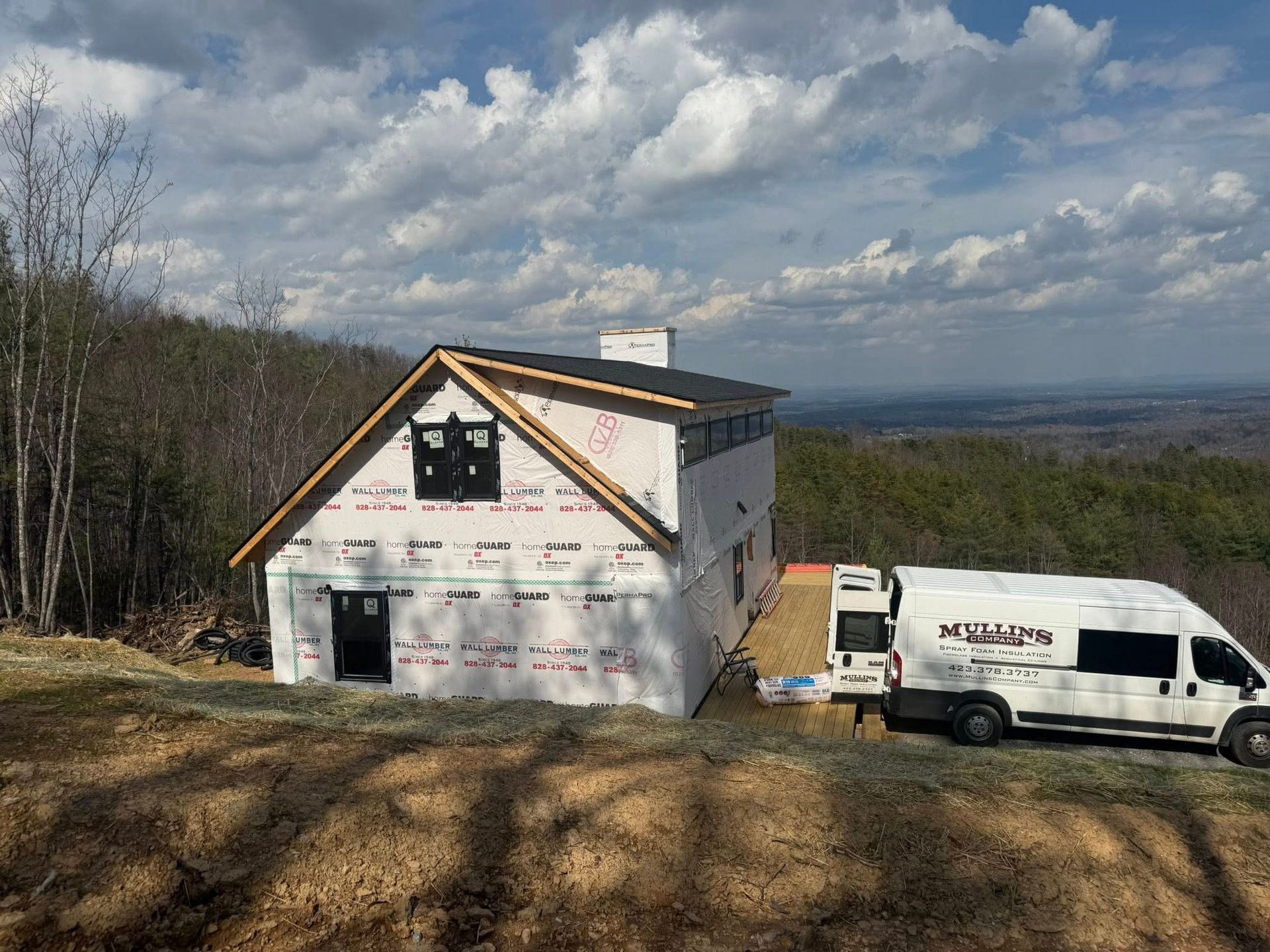 House under construction on a hill with a white work van parked beside it under a cloudy sky