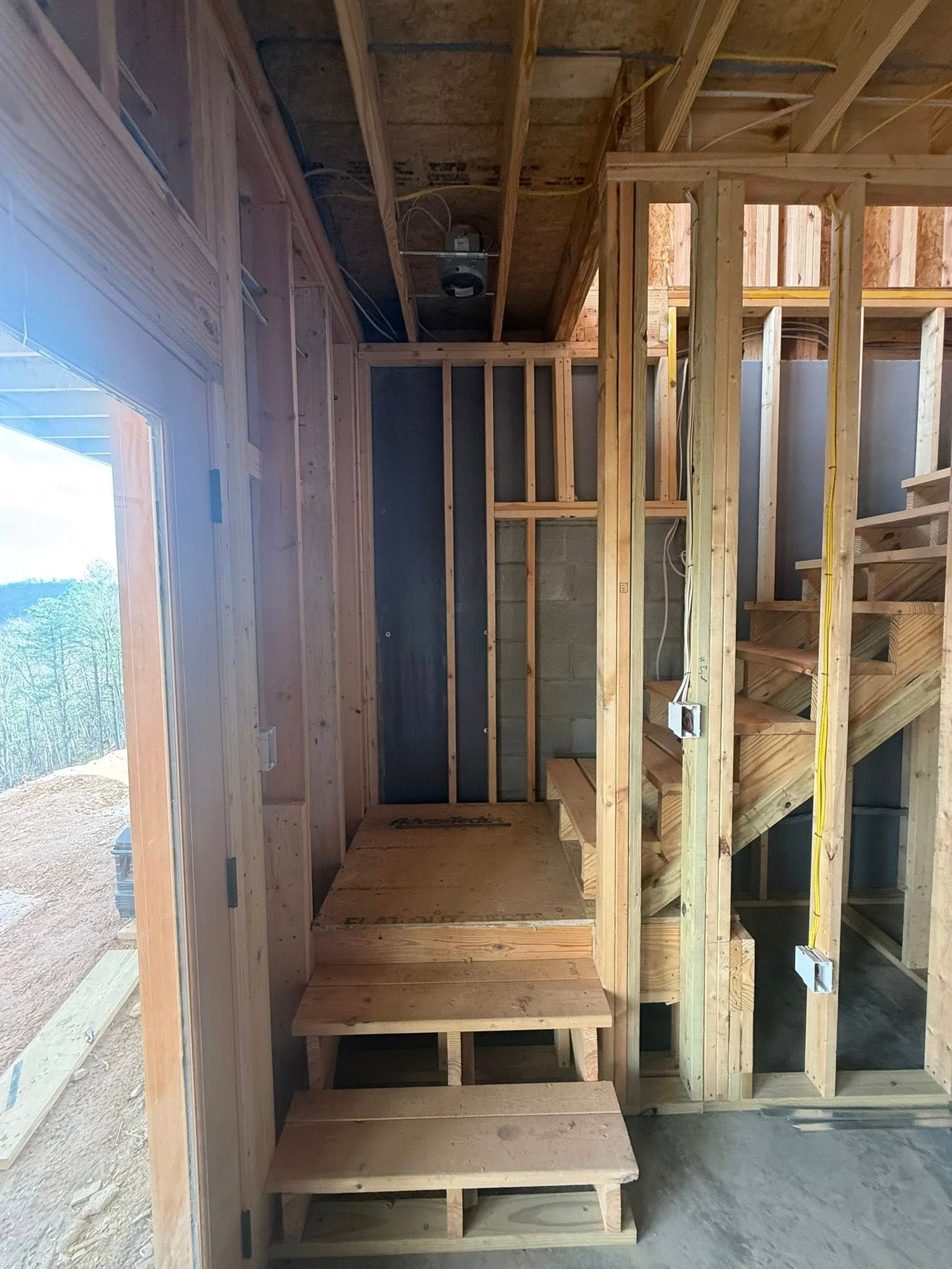 Unfinished wooden interior with stairs, exposed studs, and a window opening to the outdoors