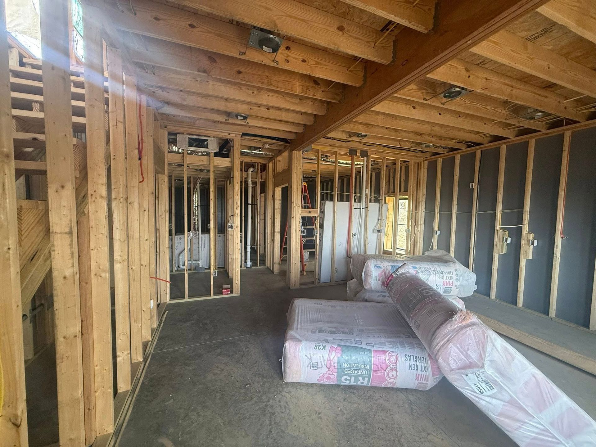 Interior of an unfinished house with exposed wooden framing, insulation rolls, and a concrete floor