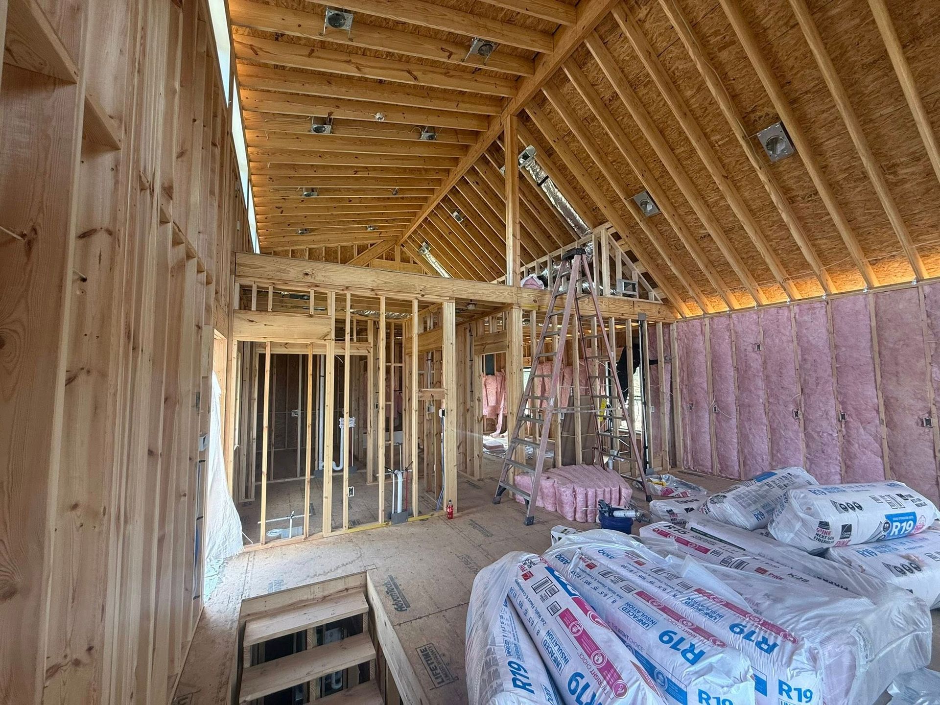 Unfinished attic framed with exposed rafters, insulation, and construction materials stacked on the floor.