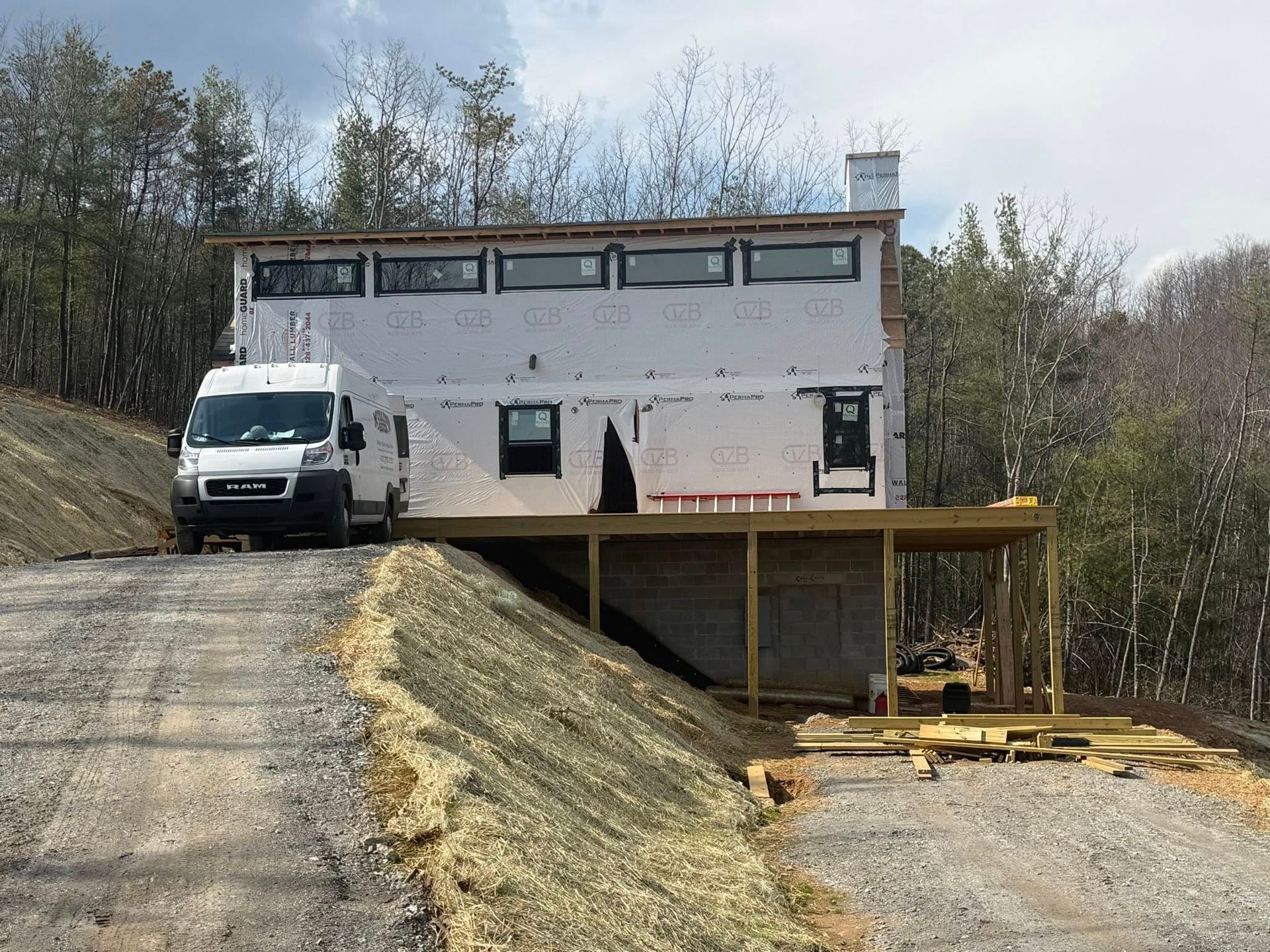 White building under construction beside a white van on a dirt slope, with a wooden deck frame in front.