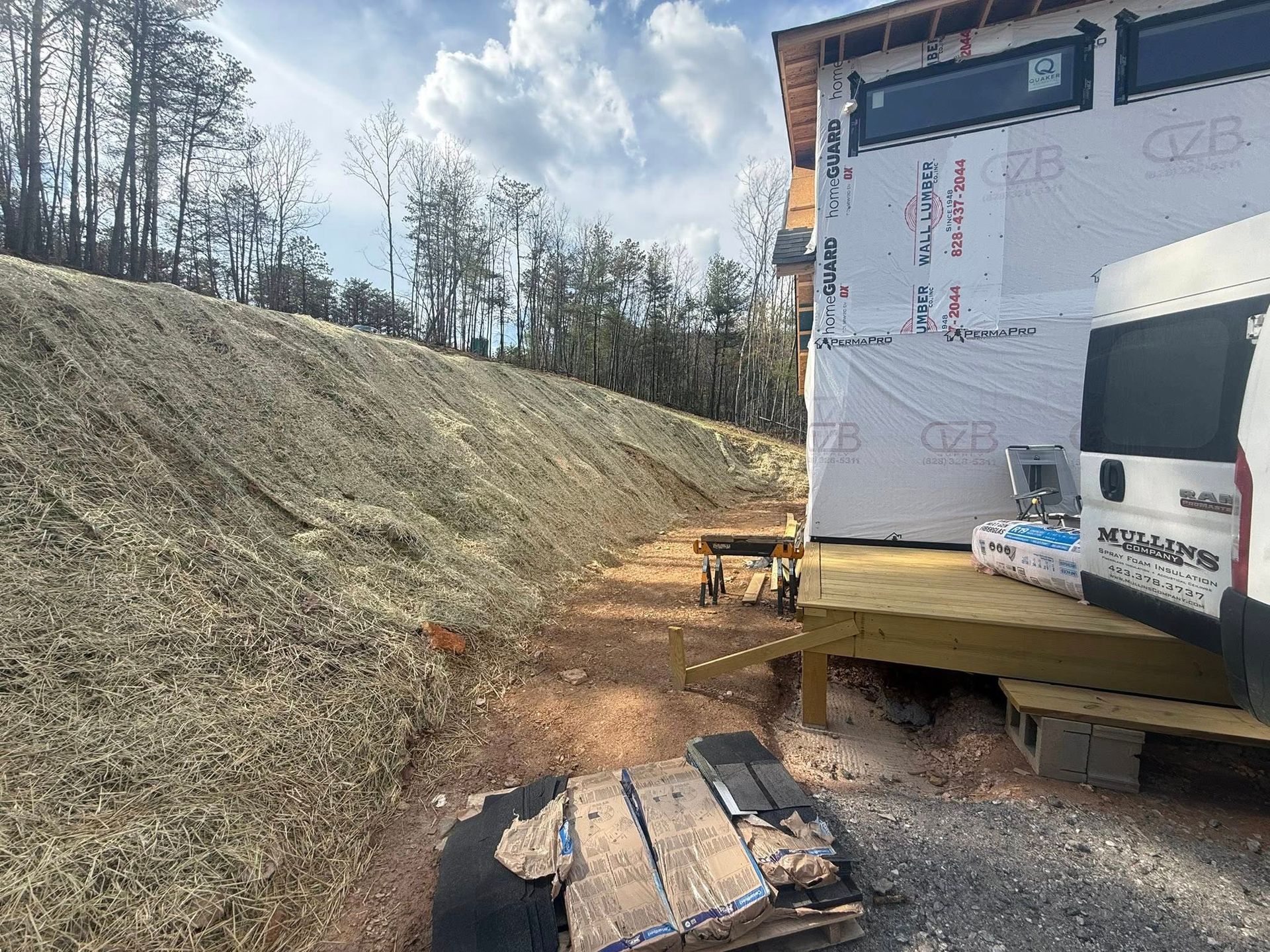 Construction site with house framing, dirt slope, and wood pallets beside a truck